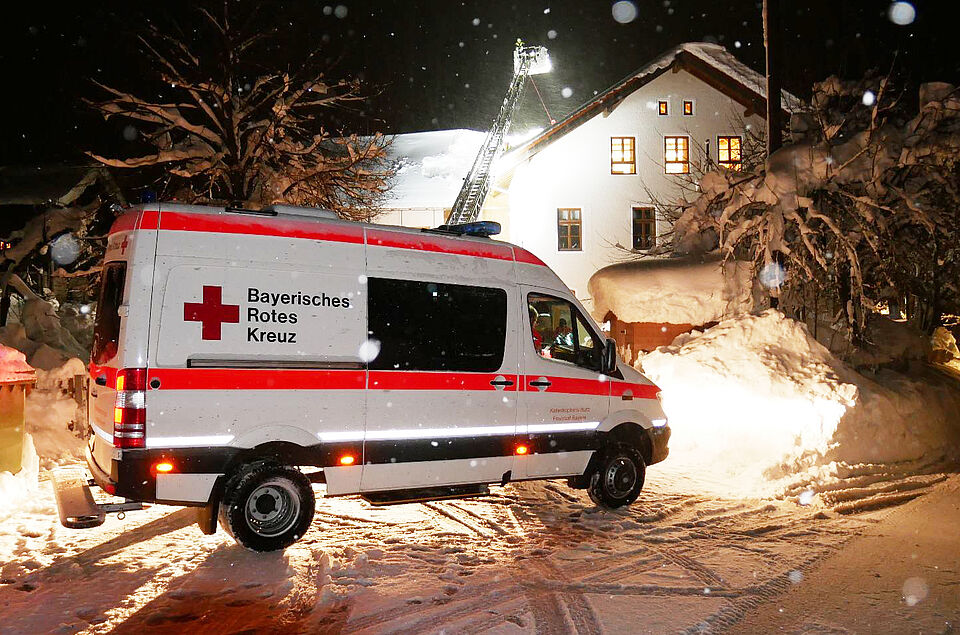 Krankenwagen des Münchner Roten Kreuzes vor Haus im Landkreis Miesbach